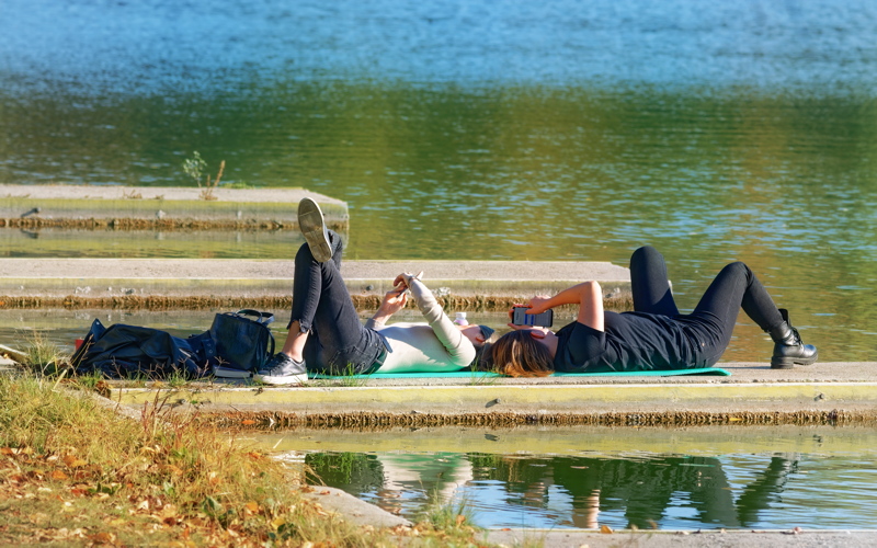 18 - Two girls relaxing by the water looking to smartphones